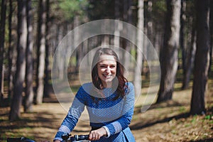 Beautiful young smiling woman with short dark hair and hat standing near bicycle with basket of huge bouquet of