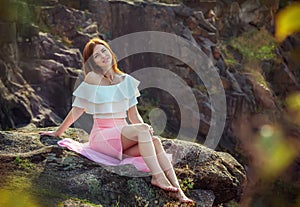 Beautiful young smiling woman sitting on a cliff