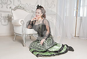 Beautiful young smiling woman wearing green medieval vintage Victorian Style dress sitting on the floor