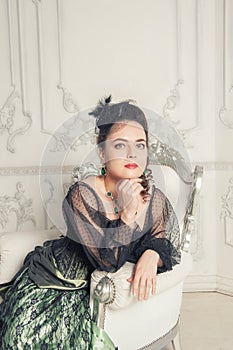 Beautiful young smiling woman wearing medieval vintage Victorian Style dress sitting in the armchair