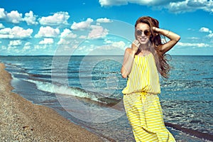 Beautiful young smiling woman wearing yellow striped baggy summer maxi dress at the seaside