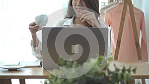 Beautiful young smiling woman working on laptop while enjoying drinking warm coffee sitting in a living room at home.
