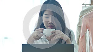 Beautiful young smiling woman working on laptop while enjoying drinking warm coffee sitting in a living room at home.