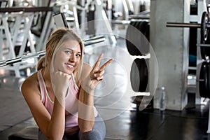 Beautiful young sport woman taking a break from exercise showing v-sign in fitness gym .girl in sportswear workout rest