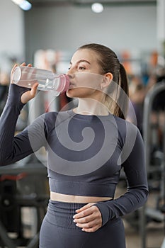 A beautiful young sports caucasian woman in gray sportswear trains in the gym.