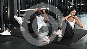 Beautiful young sports couple, african man and caucasian woman, are doing crunches at the gym.