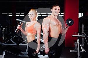 Beautiful young sporty couple showing muscle and posing with dumbbells in gym during photoshooting