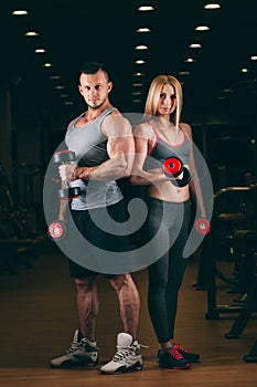 Beautiful young sporty couple showing muscle and workout in gym dumbbell