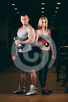 Beautiful young sporty couple showing muscle and workout in gym dumbbell