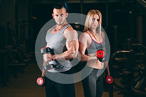 Beautiful young sporty couple showing muscle and workout in gym dumbbell