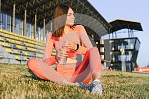 Beautiful young sporty woman drinking water after running. Fit jogger girl taking a break after sport. Lifestyle, people, sport