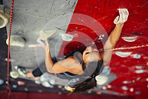 Beautiful young strong woman climbing on red artificial wall top view.