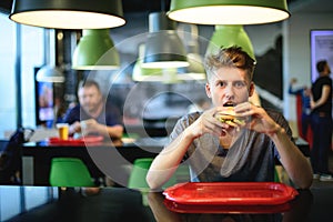 Beautiful young student eats a burger in a fast food restaurant. Tasty and harmful food. Nooning.