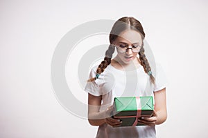 Beautiful young student girl received a long awaited gift, with surprise and joy looking at the green box on a white background