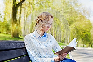 Beautiful young student girl in shirt sitting with a book in her hand in a green park