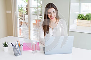 Beautiful young student woman studying for university using laptop and notebook with a happy face standing and smiling with a