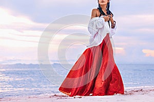 Beautiful young stylish boho woman walking on the beach at sunset