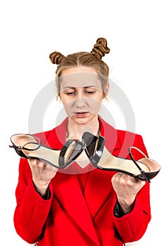 Beautiful young stylish girl disappointed, sad looks at the sandals dressed in a red coat in the hands of holding shoes