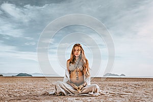 Beautiful young stylish pregnant woman with boho accessories on the beach at sunset