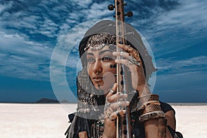 Beautiful young stylish tribal woman in oriental costume playing sitar outdoors. Close up