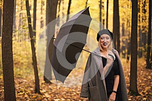 Beautiful young stylish woman with black umbrella while walking in autumn forest on rainy day