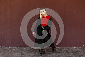 Beautiful young stylish woman in a fashionable black coat with a red shirt and black leather shoes standing and posing