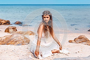 Beautiful young stylish woman sitting on sand on the beach
