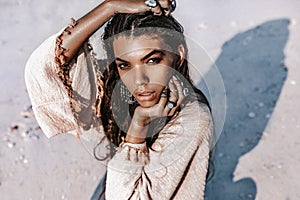 Beautiful young stylish woman with stylish boho accessories sitting on sand