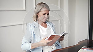 Beautiful and young successful business woman smiling with book in a cafe, reading the book. Blonde Female in blue