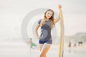 Beautiful young surfer girl stays on the beach at