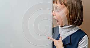 Beautiful young surprised girl looking behind white empty banner