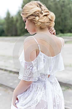 Beautiful young sweet blonde girl with wedding bouquet in the hands of the boudoir in a white dress with evening hairstyle walks