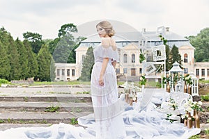 Beautiful young sweet blonde girl with wedding bouquet in the hands of the boudoir in a white dress with evening hairstyle walks