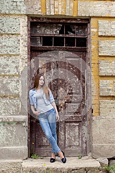 Beautiful young sweet girl with red hair in jeans standing near the door of the old city