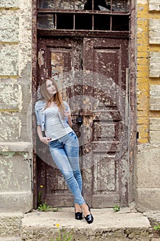 Beautiful young sweet girl with red hair in jeans standing near the door of the old city