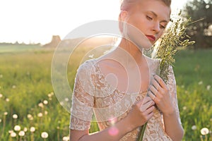 Beautiful young sweet girl in a white dress with hair on the head oblique walks in a field at sunset