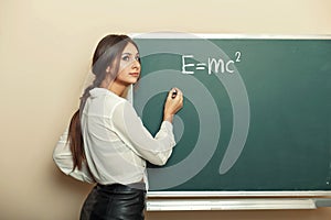 Beautiful young girl teacher writing formula on the blackboard.