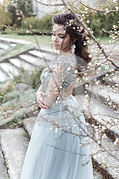 Beautiful young tender gay girl with beautiful wedding hairstyle with a snow-white smile in light dress is walking in spring