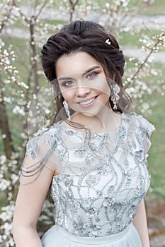 Beautiful young tender gay girl with a beautiful wedding hairstyle with a snow-white smile in a light dress is walking in a spring