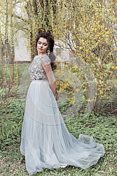 Beautiful young tender gay girl with a beautiful wedding hairstyle with a snow-white smile in a light dress is walking in a spring