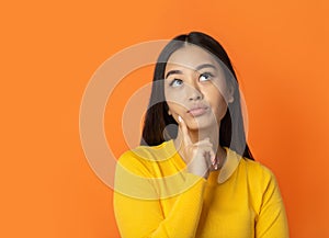 Beautiful young thinking woman thoughtful on orange background, copy space