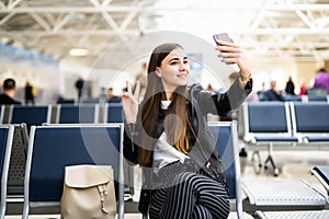 Beautiful young tourist girl in international airport, taking funny selfie with passport and boarding pass near flight information