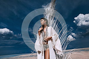 Beautiful young tribal style woman with lots of accessories and painted white palm leaf on the beach