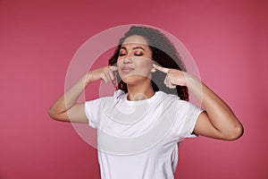 Beautiful young vietnamese woman covering her ears with palms over pink