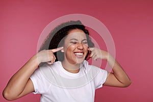 Beautiful young vietnamese woman covering her ears with palms over pink