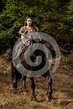 Beautiful young viking warrior woman with sword riding big black horse in the mountains scouting the land photo
