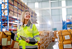 Beautiful young warehouse worker woman hold tablet and smiling also look to her left side in workplace area