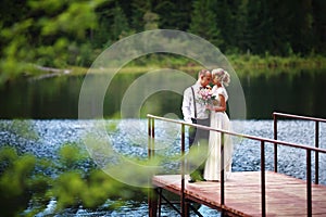 Beautiful young wedding couple, bride and groom posing on lake background. The groom and the bride on pier.