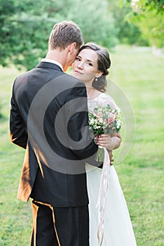 Beautiful young wedding couple in a green garden, broom`s back hugged by a nice bride