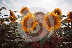 Beautiful young woman with 2 sunflowers in his hands covers his face and smiles in a field of sunflowers. Enjoy moment